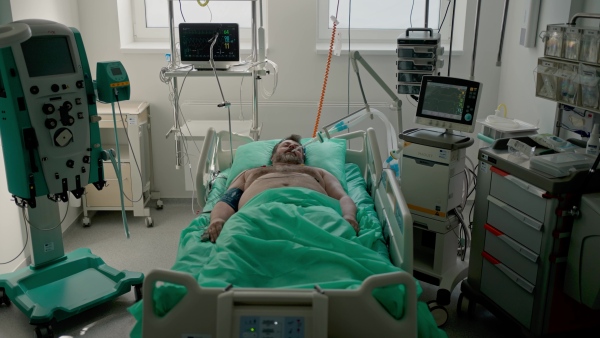 Intubated male patient lying unconscious in intensive care unit.