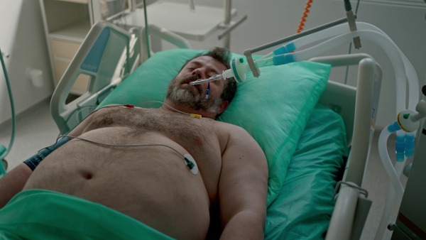 Intubated male patient lying unconscious in intensive care unit.