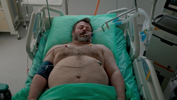 Intubated male patient lying unconscious in intensive care unit.