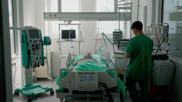 Doctor taking care of unconscious patient in hospital bed. Intensive care unit.
