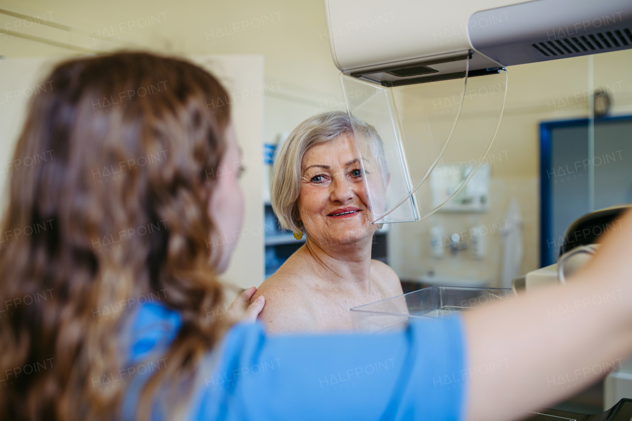 Nurse adjusts elderly patient for accurate breast imaging. Preventive breast cancer screening.