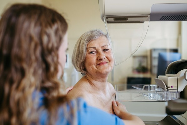 Nurse adjusts older patient for accurate breast imaging. Preventive breast cancer screening.