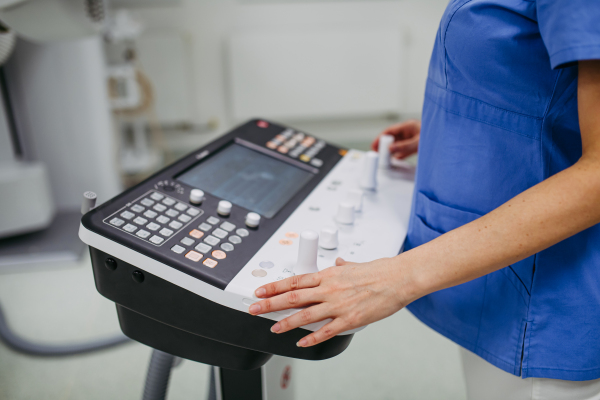 Radiologic technologist operating tilting fluoroscopy wall unit during elderly patient scan