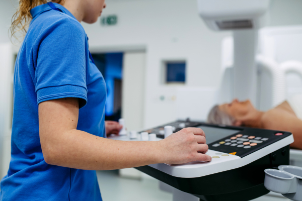Radiologic technologist operating tilting fluoroscopy wall unit during elderly patient scan