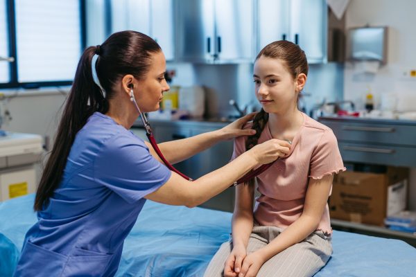 Female pediatrician listening to girl's heartbeat during routine check-up.