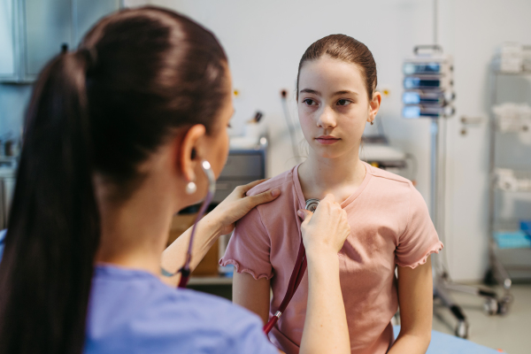 Female doctor examining sick girl with stethoscope during check-up.