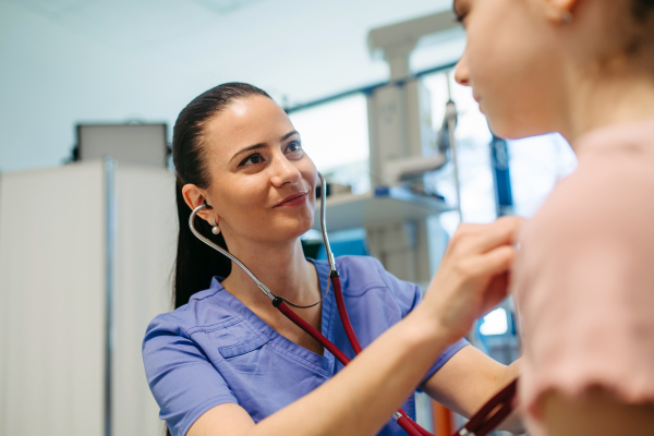 Smiling doctor examining child with stethoscope in hospital setting