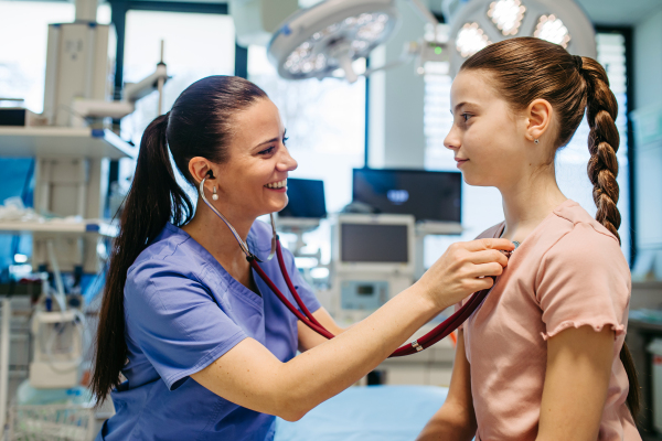 Smiling doctor examining child with stethoscope in hospital setting