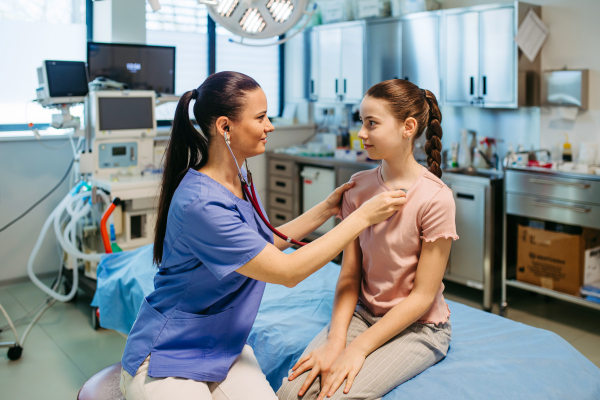 Smiling doctor examining child with stethoscope in hospital setting