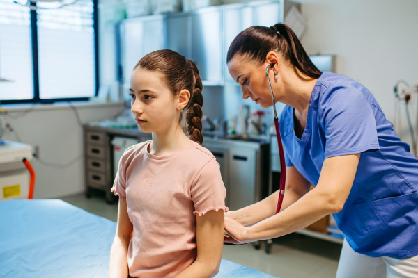 Female pediatrician listening to girl's breathing during routine check-up.