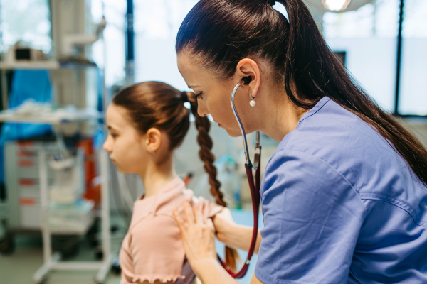 Female doctor examining sick girl with stethoscope during check-up.