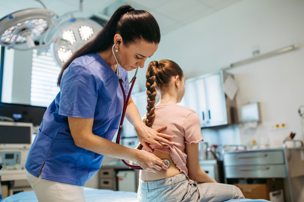 Female doctor examining sick girl with stethoscope during check-up.