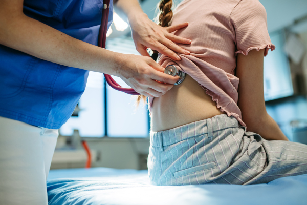 Close up of pediatrician listening to girl's breathing during routine check-up.