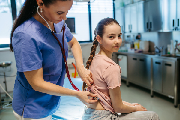 Female doctor examining sick girl with stethoscope during check-up.