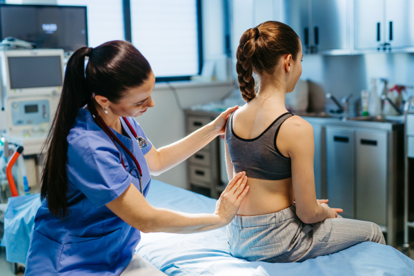 Pediatrician checking girl's spine during routine health check-up.
