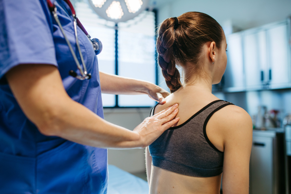 Doctor evaluating child's spine for scoliosis during check-up.
