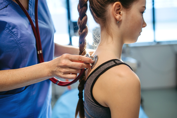 Pediatrician checking girl's spine during routine health check-up.
