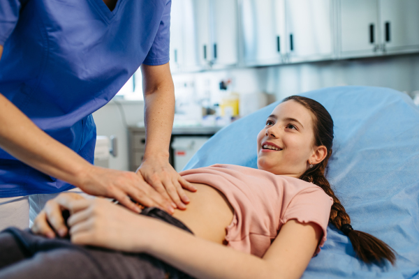 Female doctor palpating girl's abdomen during preventive checkup.