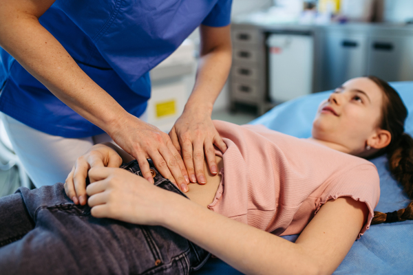 Female doctor palpating girl's abdomen during preventive checkup.