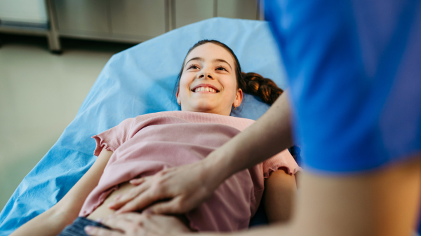 Female doctor palpating girl's abdomen during preventive checkup.