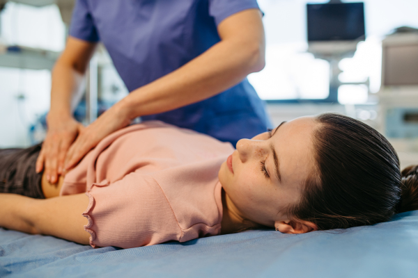 Child lying on exam table during health screening, abdominal palpation