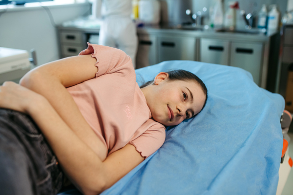 Female doctor palpating girl's abdomen during preventive checkup.