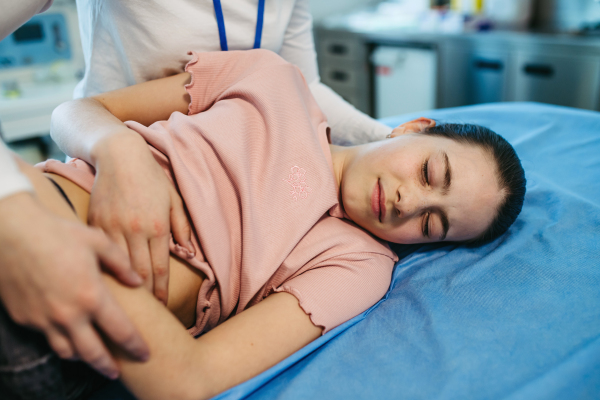 Child lying on exam table during health screening, abdominal palpation