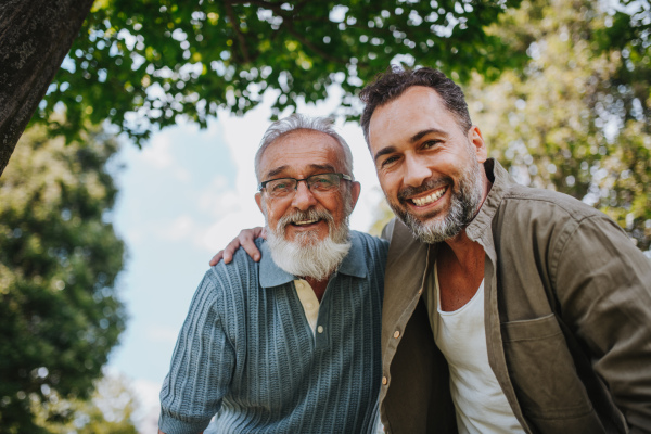 Low angle view of adult son hugging his older father. Fathers day concept.