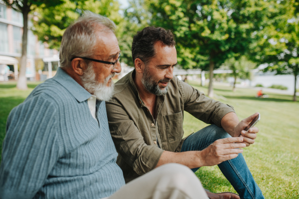 Son showing older father something in smartphone, sharing a joyful moment outdoors