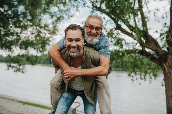 Adult son carrying older father on his back. Fathers day concept.