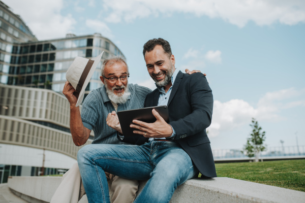 Father and adult son sharing a joyful moment, watching something in tablet. Fathers day concept.