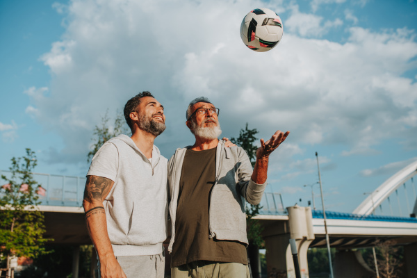 Sporty father and adult son playing football in park, throwing ball. Fathers day concept.