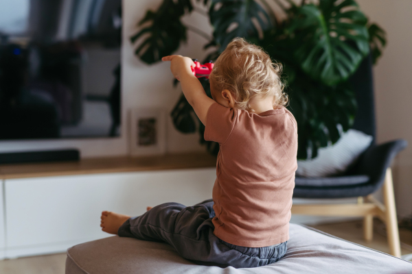 Adorable toddler is playing with a turned-off video game console.