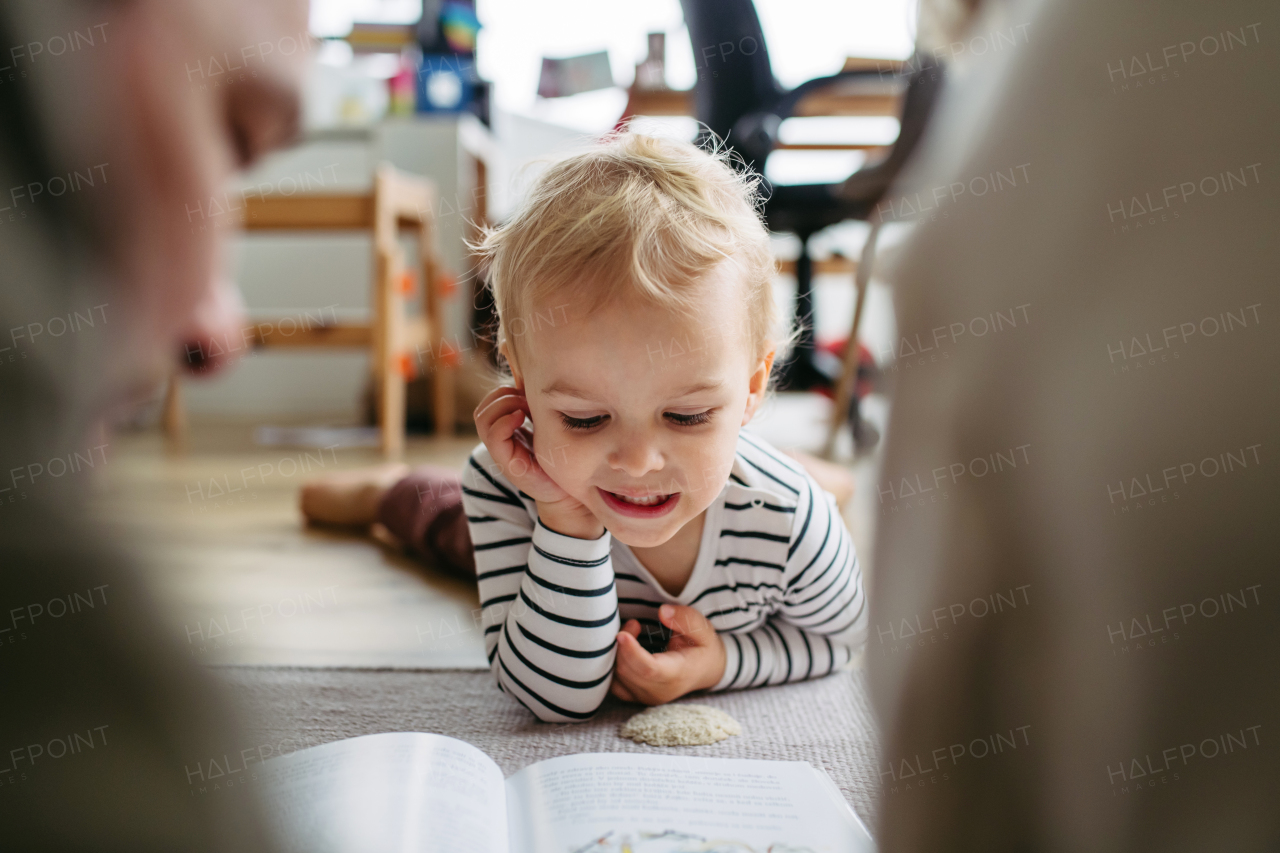 Parents reading book with little son, sitting on floor. Bonding moment.