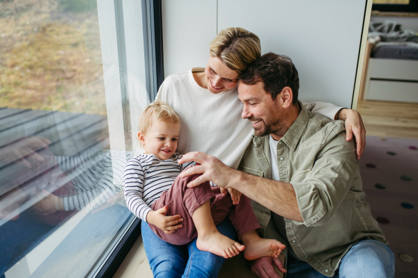 Parents playing with little son, sitting by window. Bonding moment.