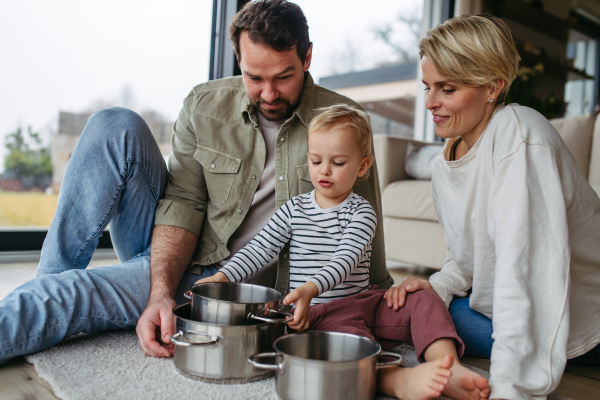 Parents and little toddler son playing drums on kitchen pots.