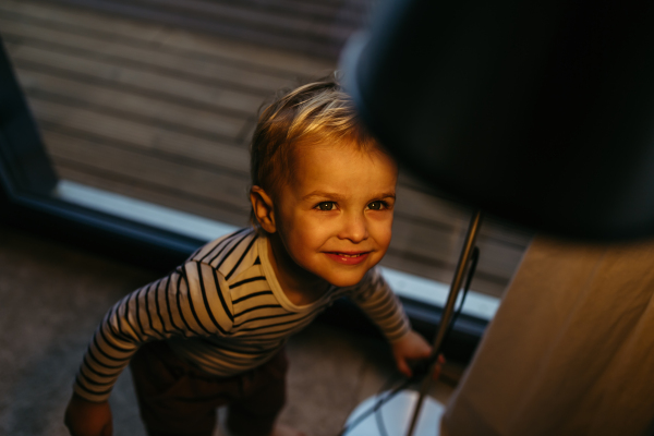 Adorable toddler boy at home, standing under lamp.