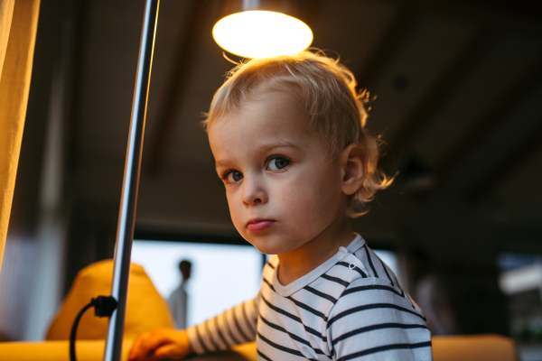 Adorable toddler boy at home, standing under lamp.