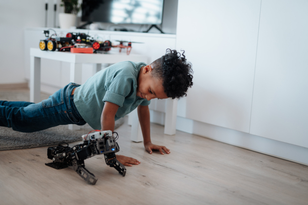 Cute boy having fun with small robot at home as part of STEM learning.