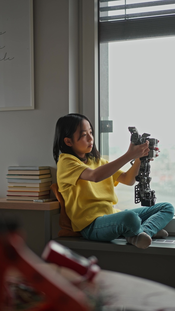 Curious young Japanese girl playing with her DIY robot at home, exploring robotics.
