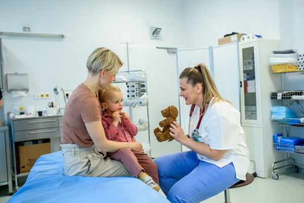 Female pediatrician comforting little boy with teddy bear during checkup