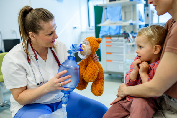 Female pediatrician demonstrates oxygen mask on teddy bear to young patient