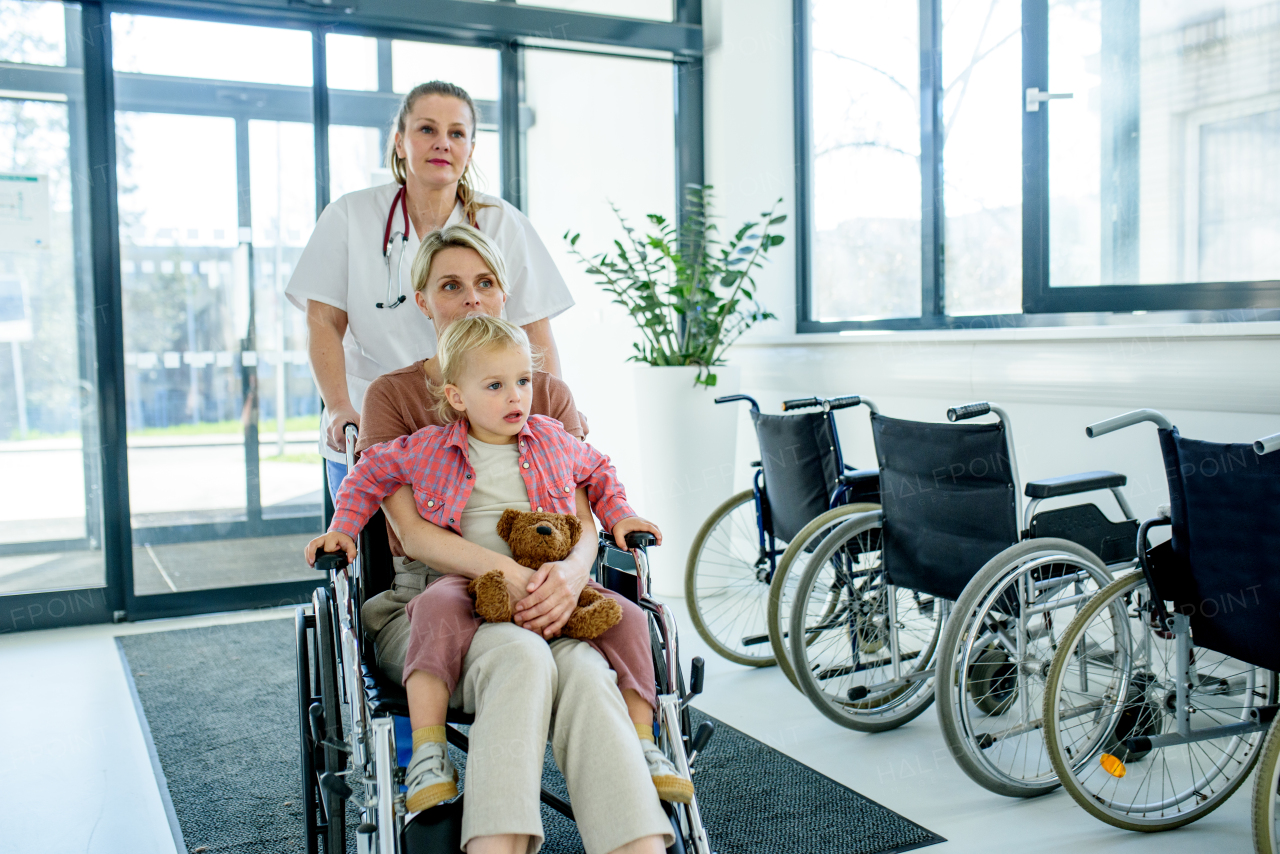 Female doctor or nurse pushing wheelchair with mother and son after treatment