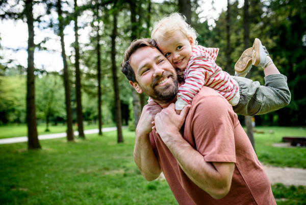 Dad carrying his smiling son on shoulders during walk in park