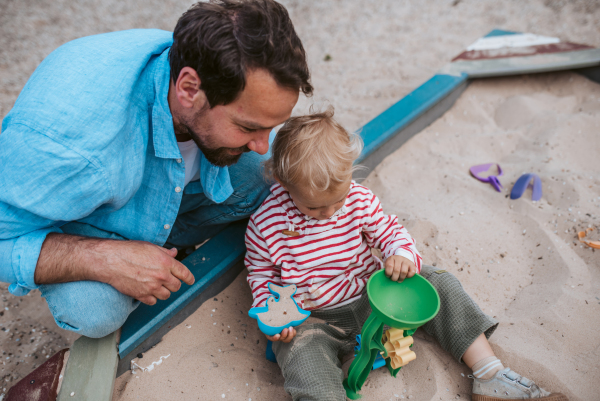 Father and little toddler son playing in the sandbox on playground, weekend fun.