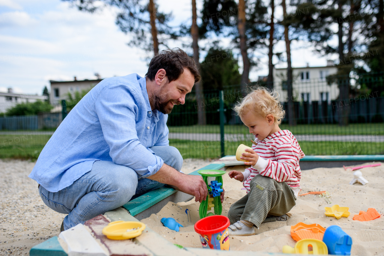 Father and little toddler son playing in the sandbox on playground, weekend fun.