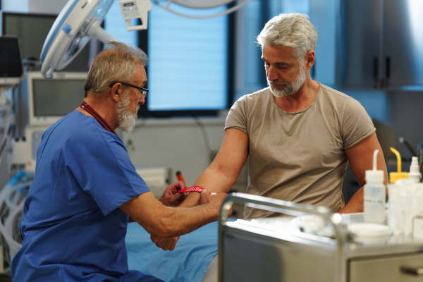 Older doctor drawing blood from patient's arm during medical examination.