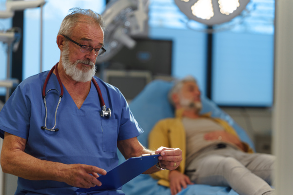 Portrait of older doctor standing in examination room in hospital.
