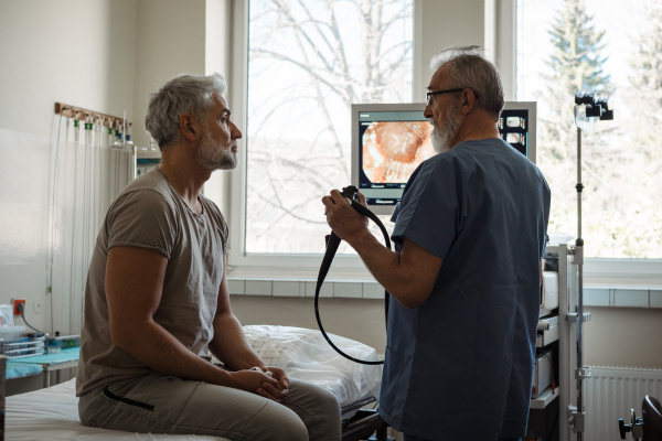 Doctor explaining colonoscopy results to patient using monitor images on screen.