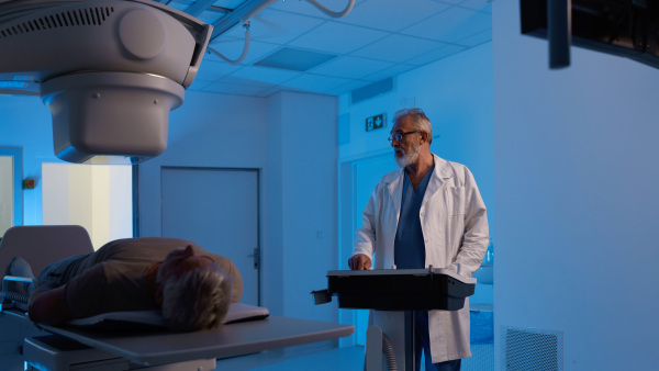 Male patient undergoing X-ray examination using a tilting radiographic wall stand.